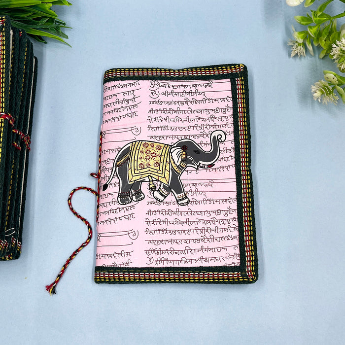 A handmade cotton paper diary with elephant print, bound with a red and black string, placed on a blue surface.