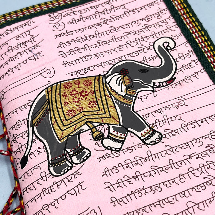 A handmade cotton paper diary with elephant print, bound with a red and black string, placed on a blue surface.