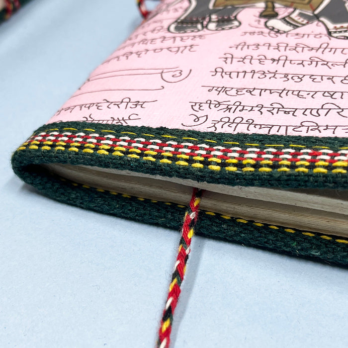 A handmade cotton paper diary with elephant print, bound with a red and black string, placed on a blue surface.